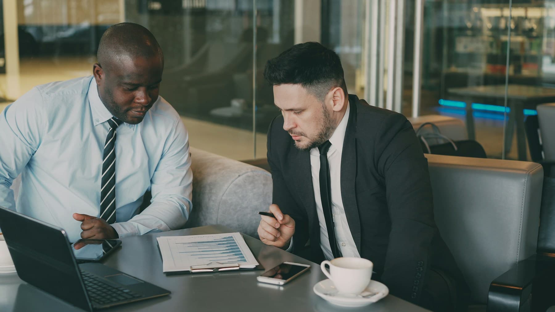 Two business professionals reviewing reports beside a laptop.